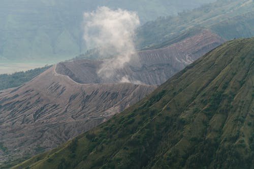 A Volcano with Smoke Beside a Green Mountain