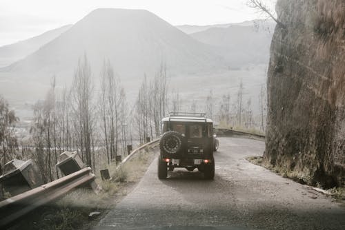 A Black Jeep Travelling on a Curved Narrow Road 