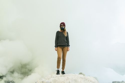 Free Individual wearing a gas mask standing amidst smoke on rocky terrain. Stock Photo