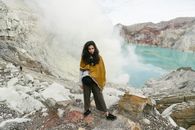 Woman in Yellow Coat Standing on Rocky Ground Near Body of Water