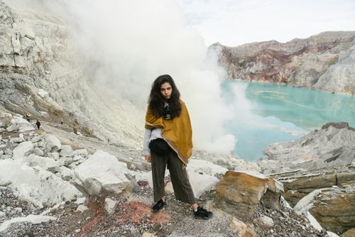 Free Woman standing in front of a fumarolic landscape with turquoise crater lake. Stock Photo