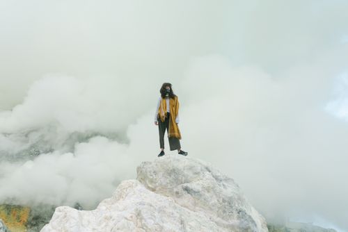 Free A woman in a mask stands on a rocky peak enveloped in misty clouds. Stock Photo