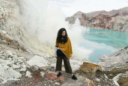 Free A woman stands near a turquoise sulfur lake in a dramatic volcanic terrain, wrapped in a yellow shawl. Stock Photo