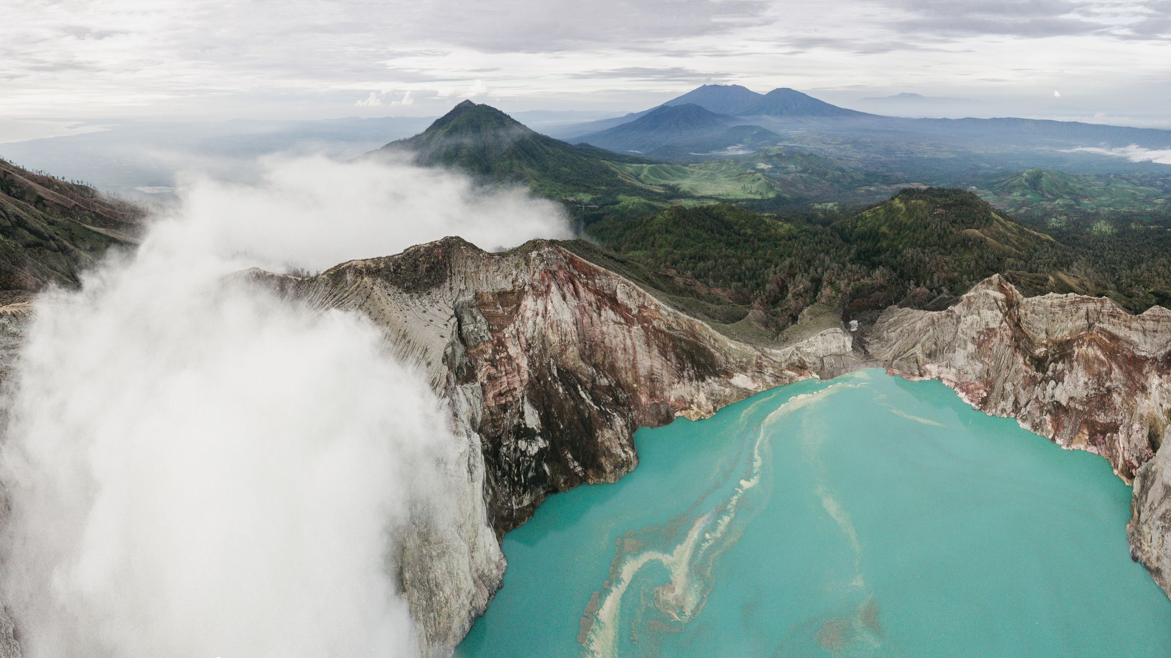 Stunning aerial view of Ijen Crater's turquoise lake surrounded by lush volcanic scenery.