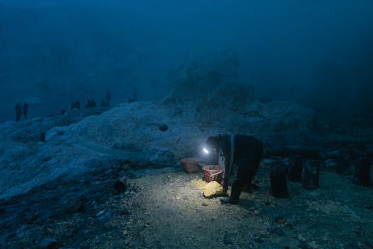 一名矿工在黑暗的采石场里用手电筒提取硫磺，营造出戏剧性的夜间场景