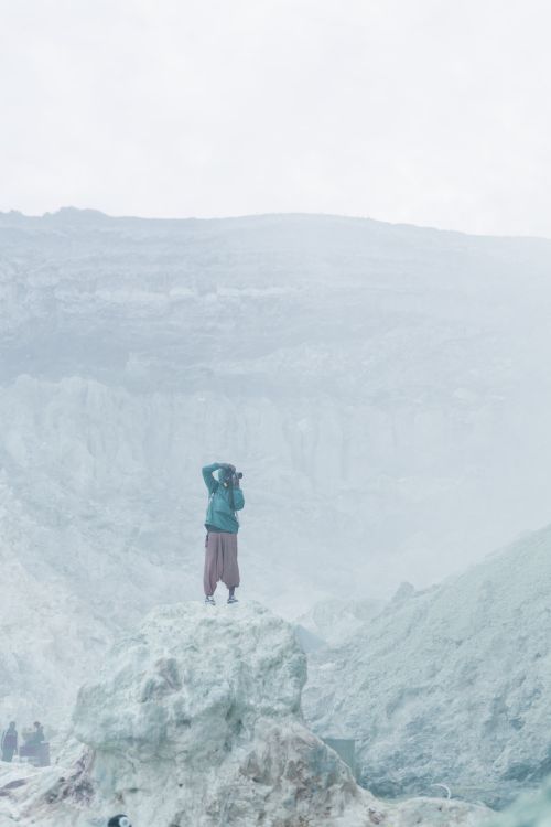 Free A solitary person on a rock capturing a misty mountain view, creating an ethereal scene. Stock Photo