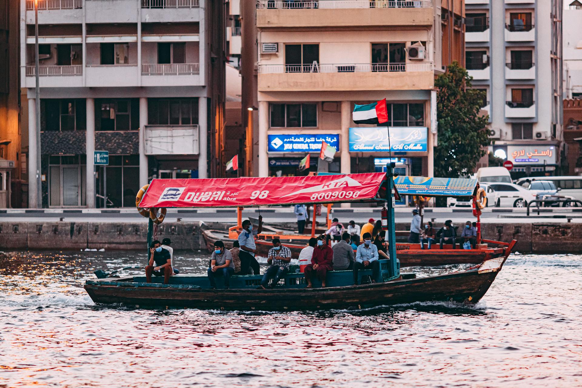 Passengers on an Abra boat crossing Dubai Creek during sunset, showcasing urban life and tradition in Dubai.