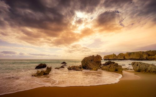 Free Scenery view of glowing sky with clouds above wavy ocean near sandy coast and stones at sundown Stock Photo
