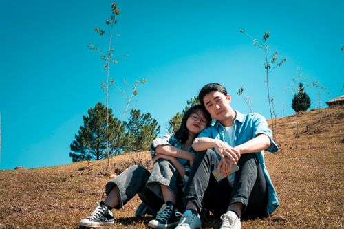 Free From below of young Asian couple sitting on meadow in nature together in sunny day under blue sky Stock Photo