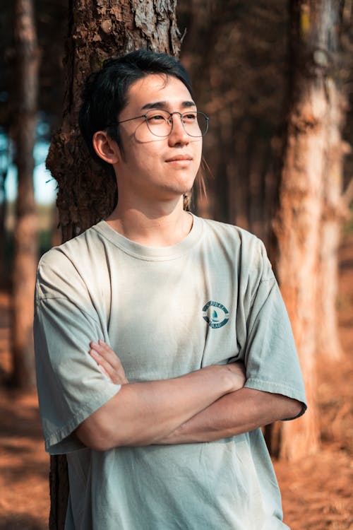 Calm young Asian man enjoying sunny day in forest