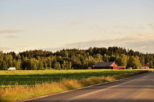 Free Beautiful rural landscape featuring a red barn, fields, and a forest under a soft dusk sky. Stock Photo