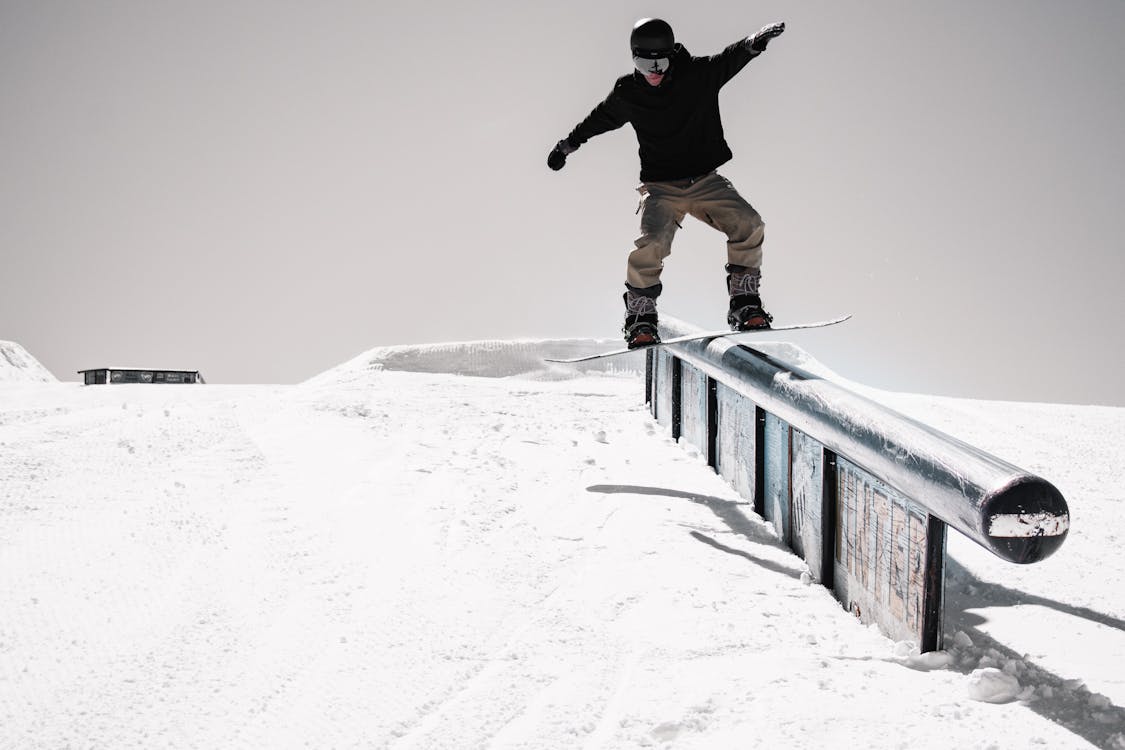 Man in Black Jacket Snowboarding on Metal Railing