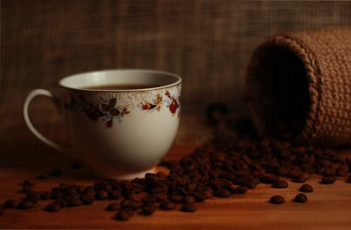 Free Ornate coffee cup surrounded by scattered coffee beans on a wooden surface. Stock Photo