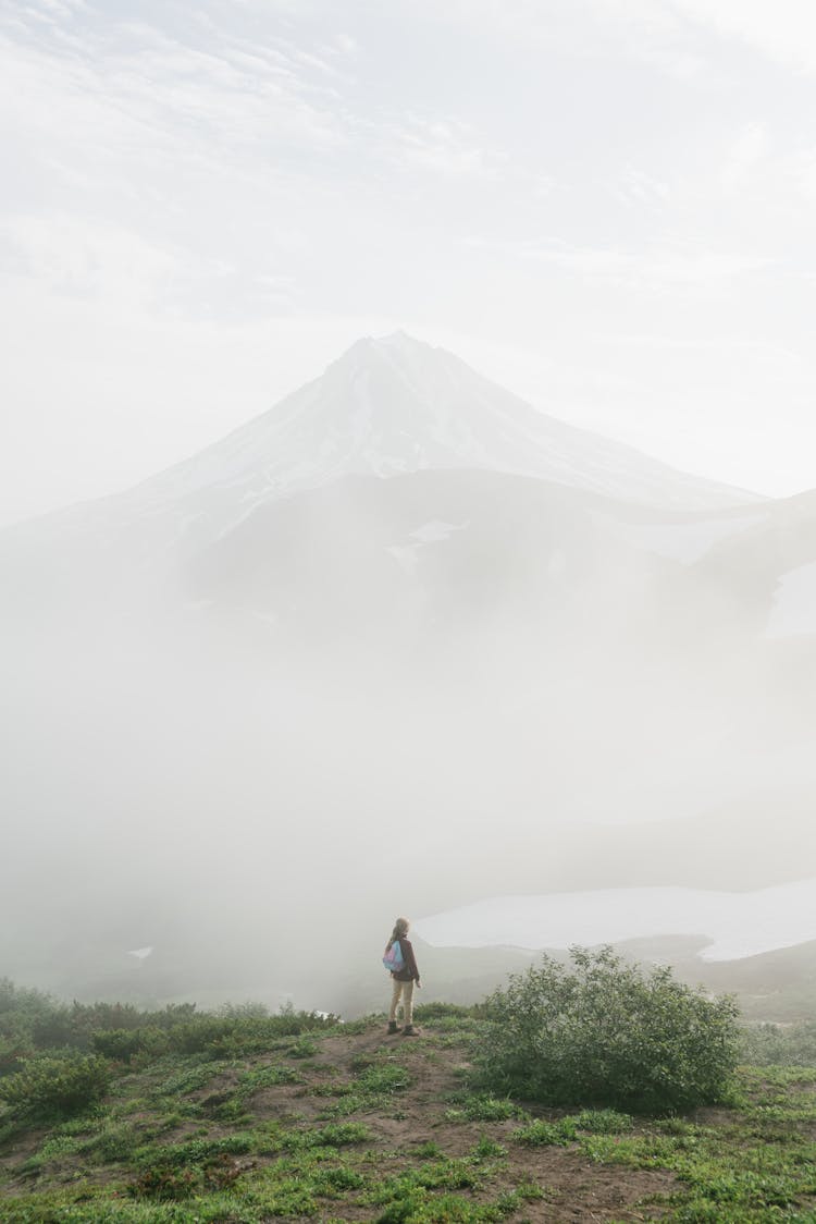 Person Standing On Green Grass Near Thick Fog