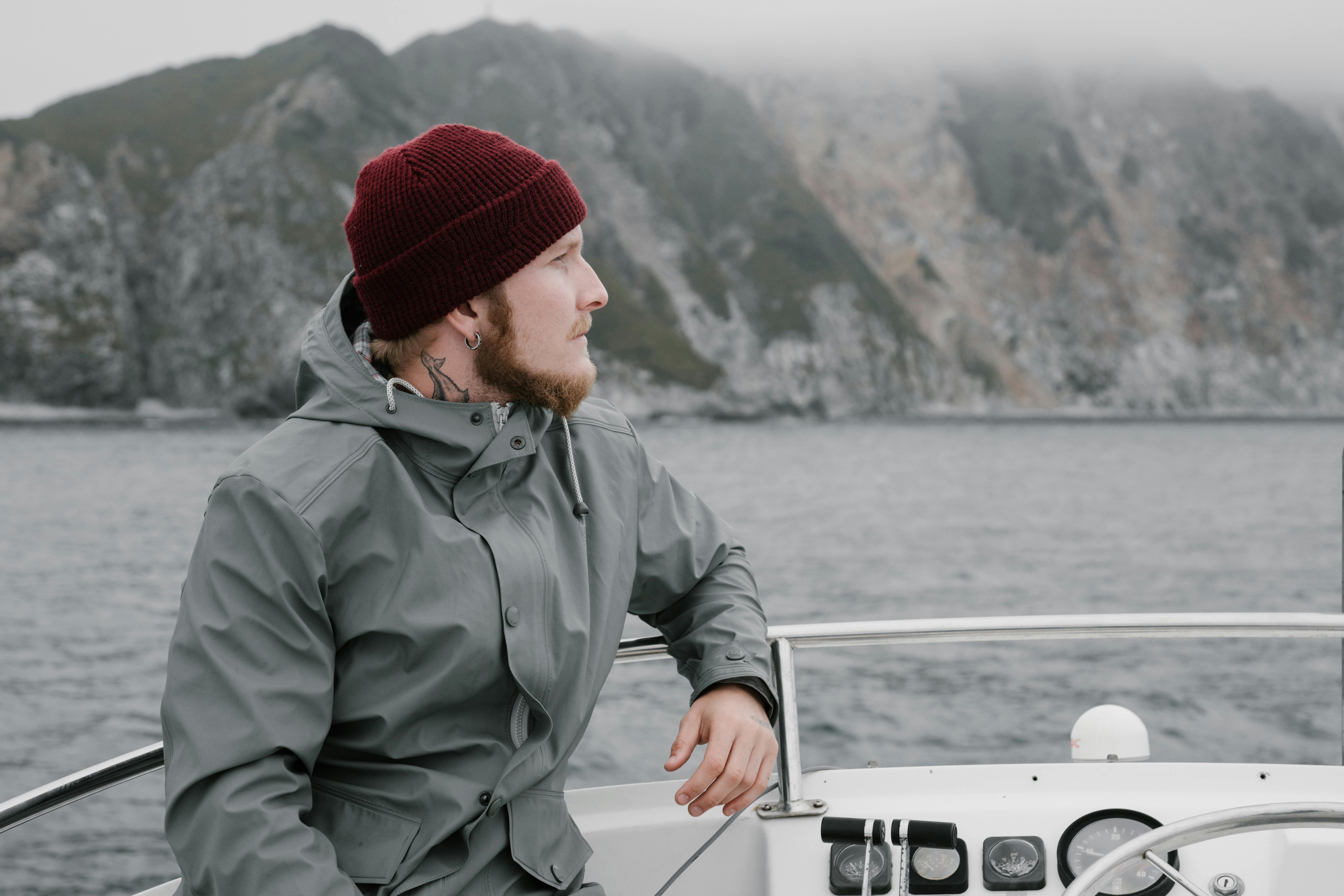 Man with beard and knit cap on boat with foggy cliffs in background.