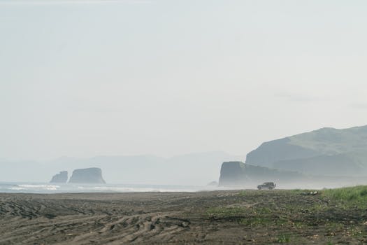 A scenic view of a misty coastline with rugged cliffs and a distant vehicle.