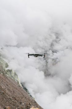 A drone soaring through dense clouds over rugged mountain terrain, capturing stunning aerial views.