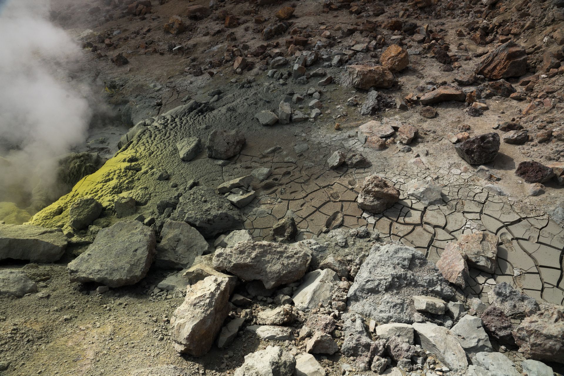 Dramatic view of a sulfur fumarole with cracked earth and rocky terrain, exuding geothermal steam.