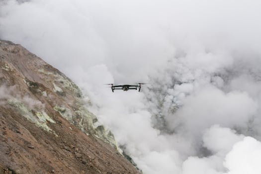 A drone navigates through a mist-covered mountainous area, showcasing rugged terrain and thick clouds.