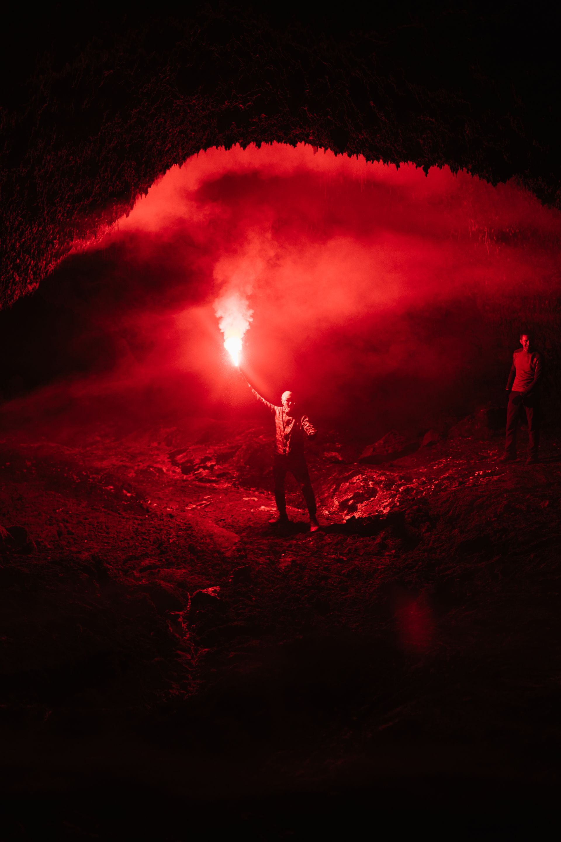 Two figures illuminate a cavern with a red flare