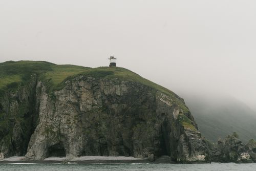 Free A lighthouse stands atop a foggy cliff, guiding ships along the rugged coast. Stock Photo