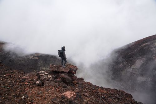 Free A solitary hiker stands on a rocky ledge surrounded by mist and rugged mountain landscape. Stock Photo