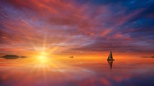 Amazing scenery of lonely sailboat floating on calm sea water reflecting picturesque colorful sunset sky
