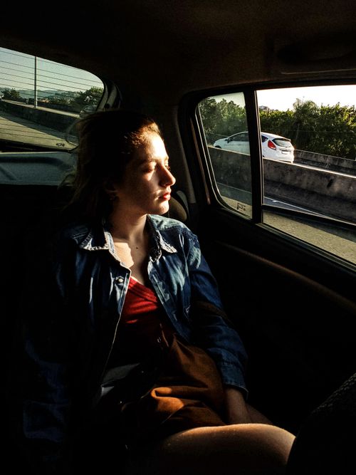 Free A young woman in a denim jacket sits in a car with sunlight streaming through the window, creating a serene scene. Stock Photo
