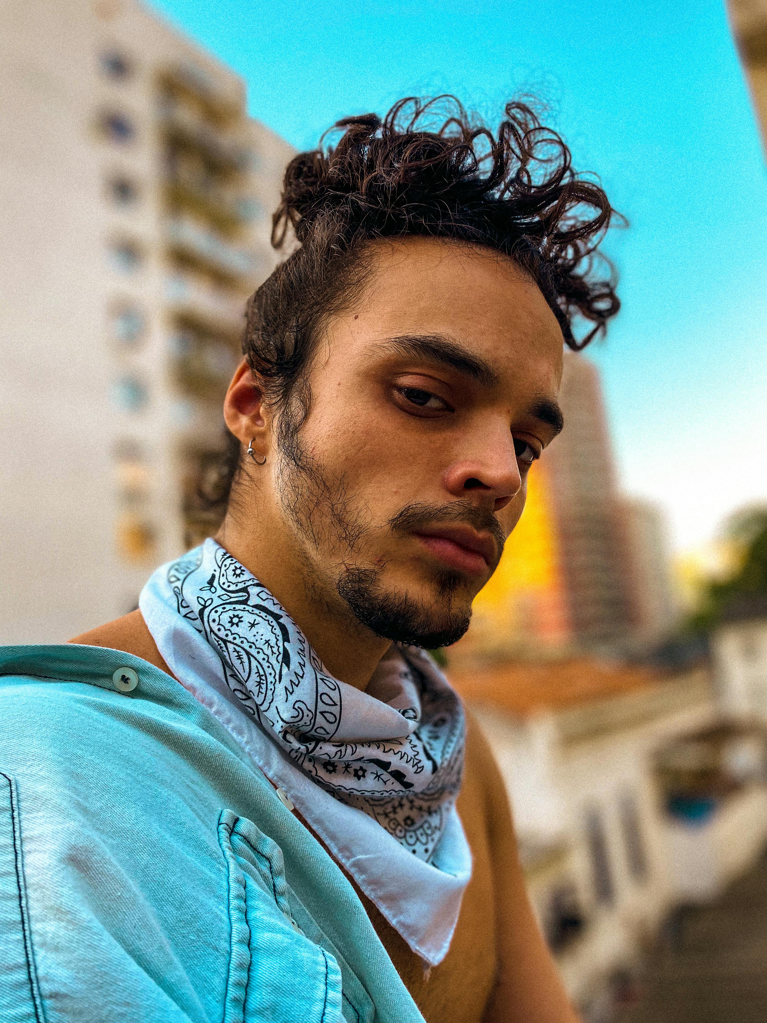 Close-up portrait of a man with curly hair and bandana in urban Rio de Janeiro setting.