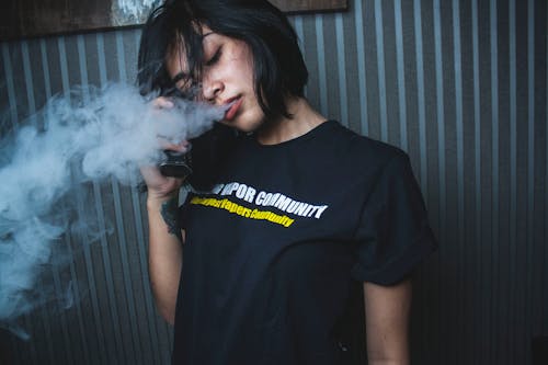 Thoughtful young woman vaping in dark room