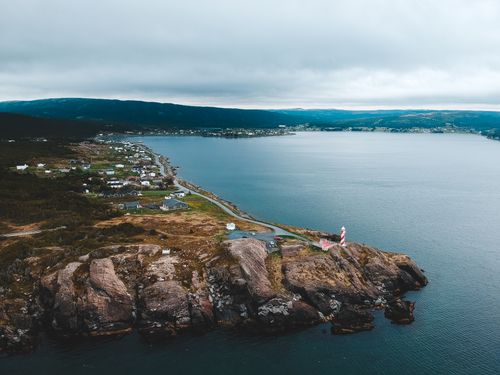 Free Drone view of beacon near road and dwelling houses on mountain near sea under cloudy sky Stock Photo