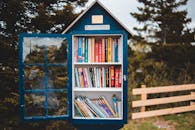 Wooden house shaped public bookcase with opened door filled with books and located in lush green park