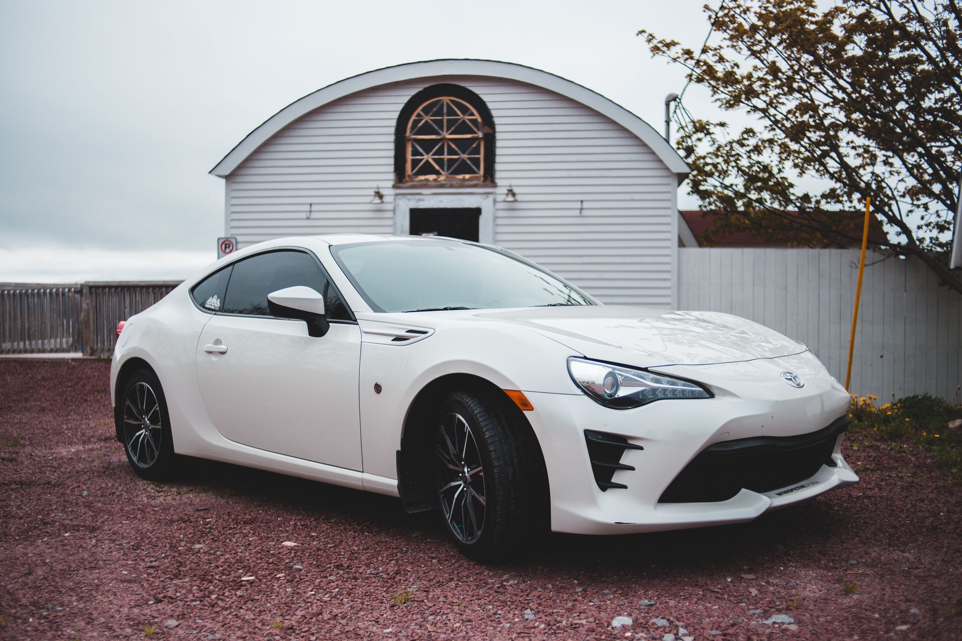 Modern powerful three banger automobile of white color parked on gravel ground near small cottage in countryside