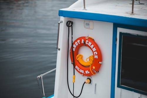 Modern small vessel with red lifesaver ring on wall floating on rippling river water in daylight