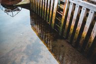 From above shabby wooden pier pilings covered with moss and reflecting in calm lake water near small boat
