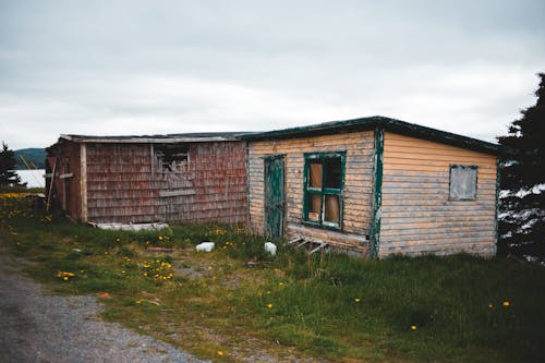 Exterior of obsolete abandoned cottages with wooden shabby walls located on grassy riverside against gloomy overcast sky