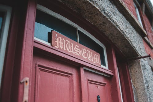 Small red signboard with curvy word Museum placed above red entrance door of brick building