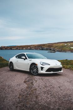 Contemporary powerful car of white color parked on gravel lake coast on cloudy day