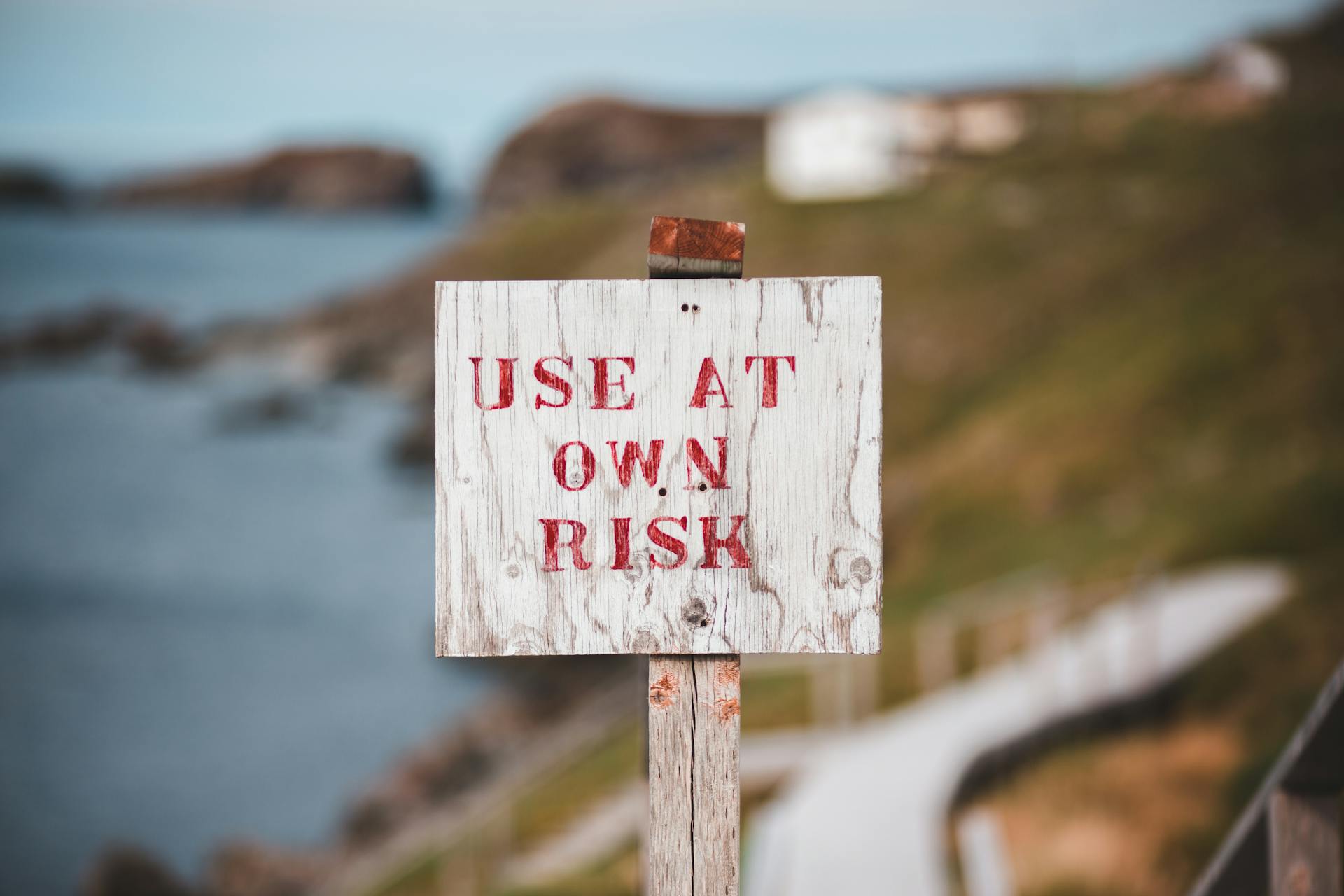 Sign with text Use At Own Risk on rocky seacoast