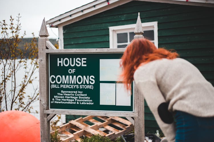 Woman Reading Signboard Outside Rural Cottage