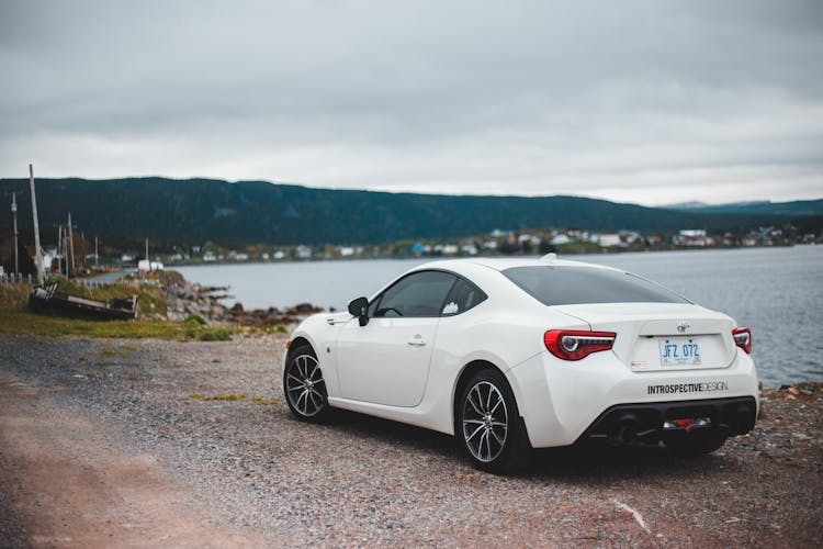 Contemporary White Car Parked On Lake Shore In Countryside