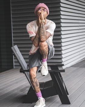 A fashionable young man wearing trendy casual apparel, sitting thoughtfully on a terrace with a modern vibe.