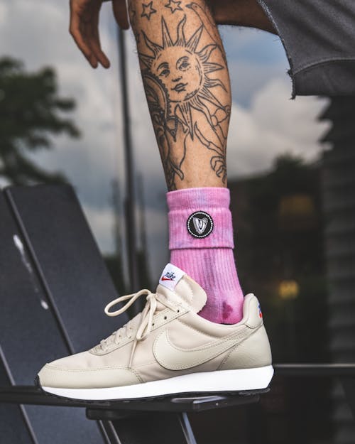 Free Crop tattooed leg of anonymous man in trendy sneakers and pink socks leaning on knee Stock Photo