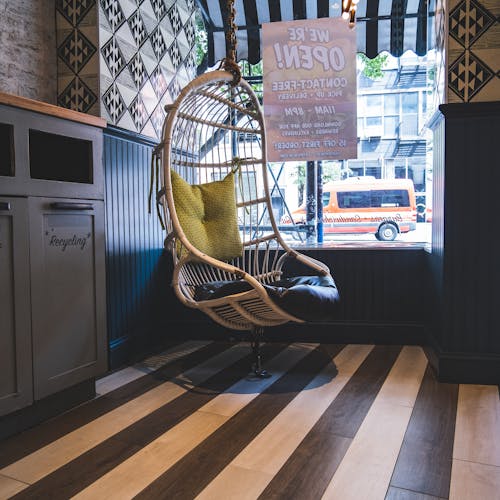 Interior of cozy cafe with wicker hanging egg chair with pillows near window