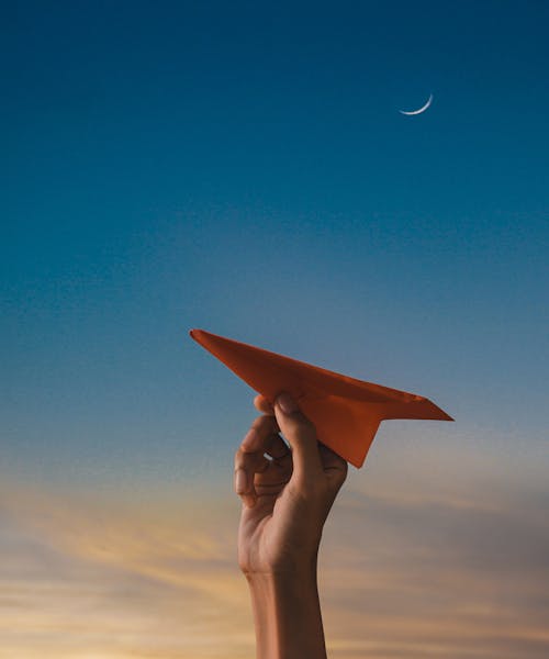 Hand Holding Paper Plane with Clear Sky behind