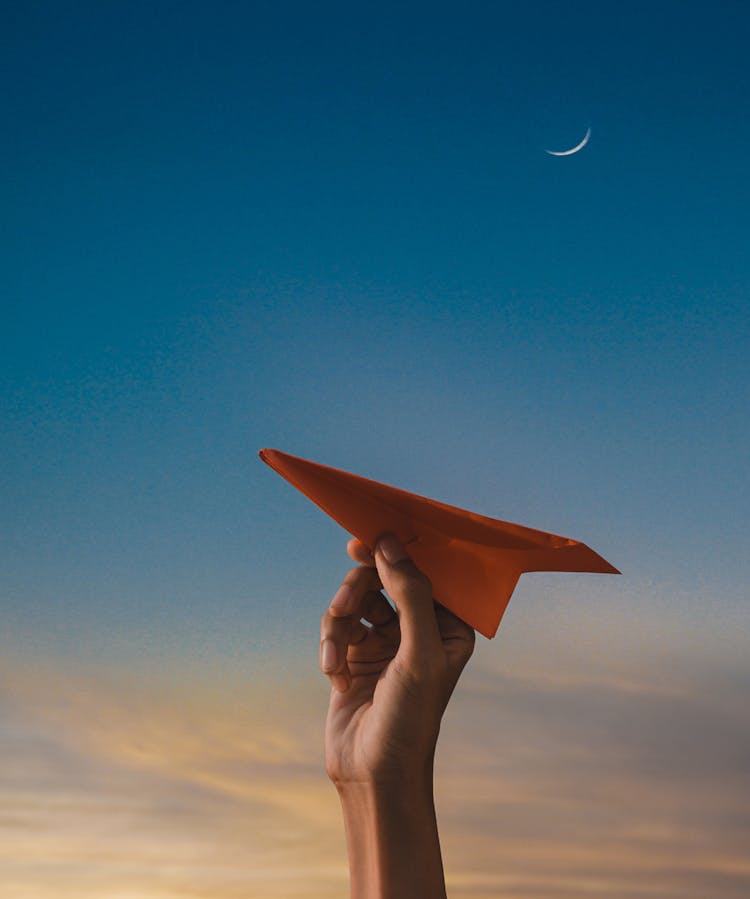 Hand Holding Paper Plane With Clear Sky Behind