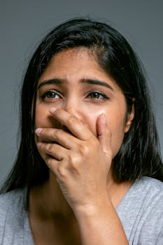 Close-up of a woman with hand over mouth, expressing emotion in a studio setting.
