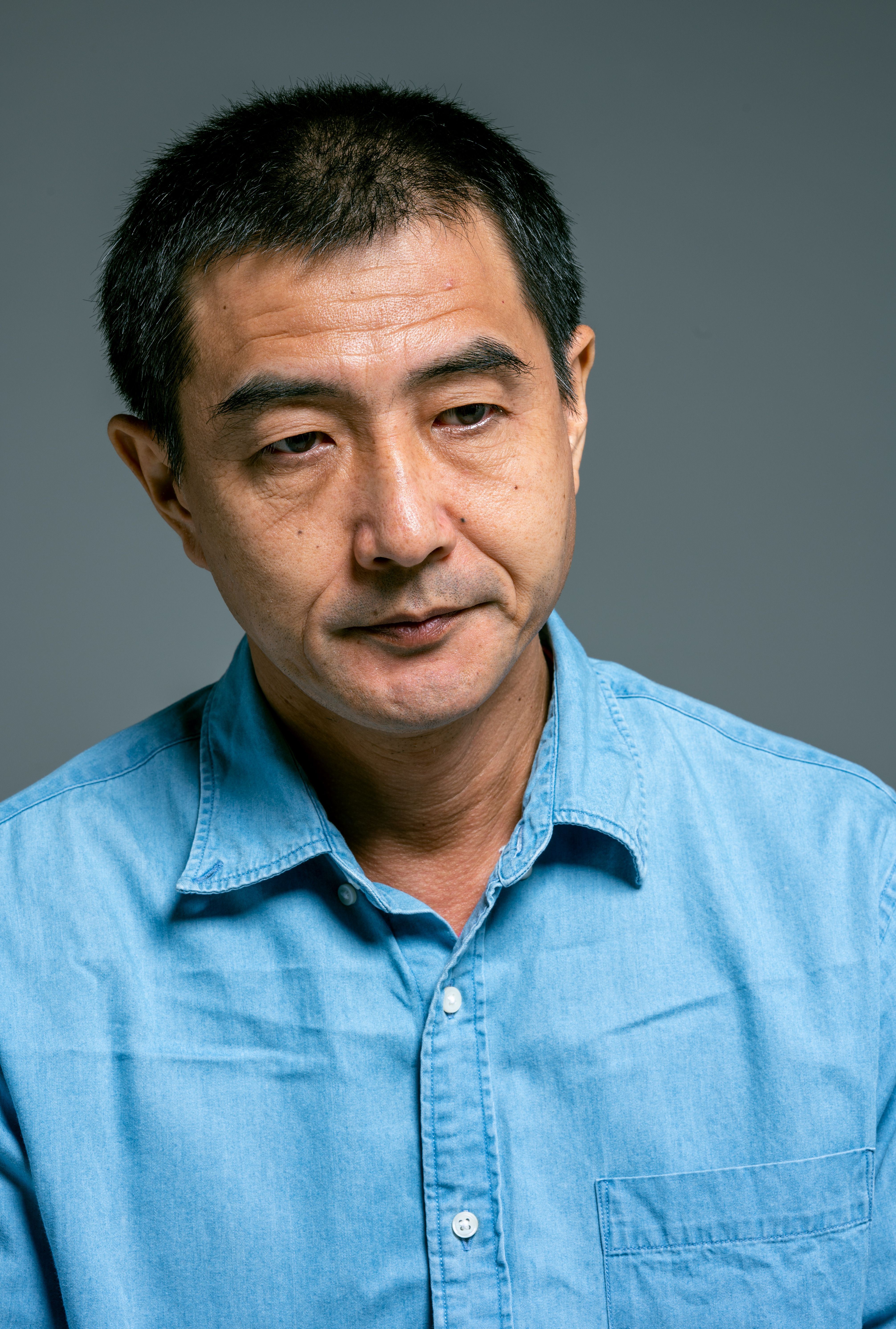 Portrait of a middle-aged Asian man wearing a blue shirt, captured in a studio setting.