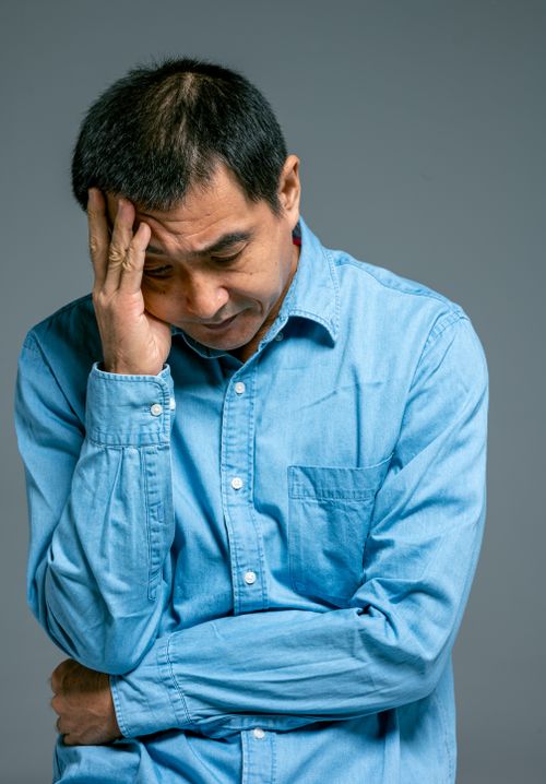 Free Asian man in a blue shirt looks downward in a contemplative pose. Stock Photo