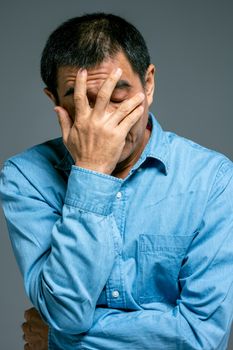 一名身穿蓝色牛仔衬衫的亚洲男子用手捂住脸，显得压力重重或忧心忡忡